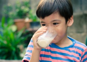 Boy drinking a full glass of milk representing the global dairy impact