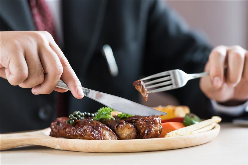 A person cutting a steak and getting ready to eat a bite